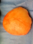 8 inch in diameter, round, flattish, yellow-orange mass on a blue surgery towel.  It feels and looks like a surgical breast implant.